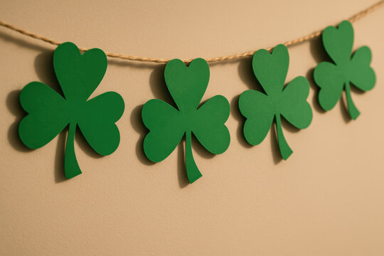 Green shamrock clover garland hanging on beige wall, festive st patrick's day holiday decoration, four paper leaves