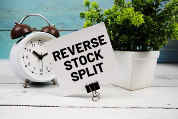Reverse Stock Split text written on paper card with alarm clock on wooden background