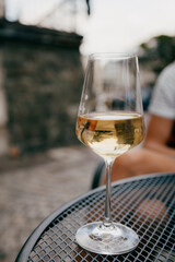 Glass of chilled white wine sits on metal table, reflecting surrounding outdoor setting, creating relaxed and inviting atmosphere. Chilled white wine glass resting on metallic surface. Wine tasting