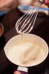 Whisk with drops of bechamel sauce preparing on a pan. Homemade bechamel sauce ready to cook italian lasagna.