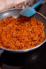 Mince meat with chopped carrots and homemade tomato sauce cooking on frying pan on induction stove. Cooking delicious dish with fresh mince meat, vegetables and tomato sauce at home.