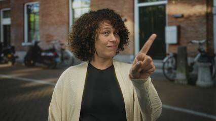 Woman points finger to chest while saying no on a city street in front of a building; rejection personal boundary.