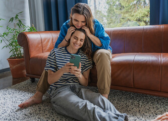 Happy lesbian couple relaxing on couch taking selfie together at home