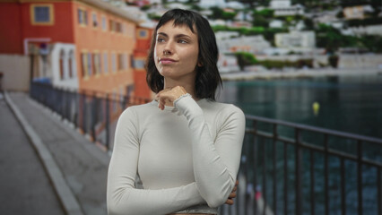 Young hispanic woman with hand on chin gesture on a colorful street lined with buildings; quiet reflection.