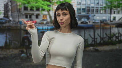 Young hispanic woman pointing finger at camera on street in amsterdam with direct gaze; vigilance...