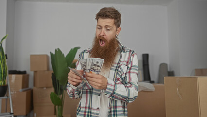 Man smiling and counting cash with bare hands in a building cluttered with boxes; financial...