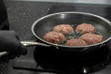 Raw cutlets sizzling and frying in a sleek modern pan with hot oil on an induction cooktop, highlighting delicious home meal preparation
