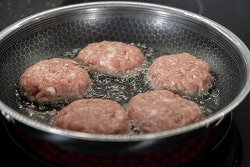 Five uncooked meat cutlets sizzling and bubbling in hot oil within a textured frying pan, demonstrating active cooking for a delicious homemade meal preparation