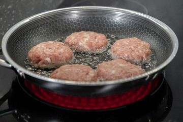 Fresh raw meat cutlets sizzling in hot oil within a patterned frying pan on an induction cooktop, symbolizing delicious homemade meal preparation and cooking