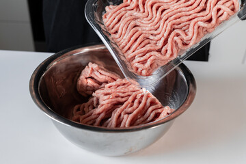 Minced poultry meat transferred from plastic packaging into a stainless steel bowl, preparing for...