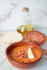 Traditional Spanish salmorejo soup with ham, egg, tomato, bread and olive oil on white marble table