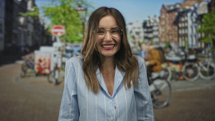 Smiling woman in blue shirt with glasses and broad grin finger pointing to sunlit canal on street; carefree joy.