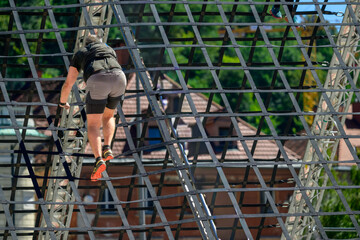 Male Athlete Climbing Outdoor Obstacle Course Under Bright Sunlight During Adventure Challenge at Urban Setting with Trees and Rope Structure