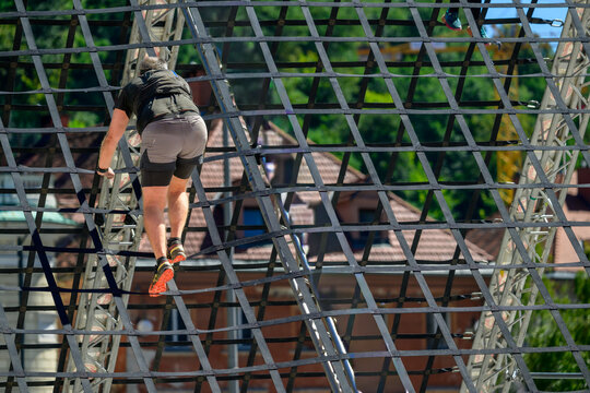 Male Athlete Climbing Outdoor Obstacle Course Under Bright Sunlight During Adventure Challenge at Urban Setting with Trees and Rope Structure