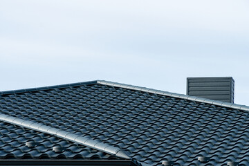 New dark grey wavy roof tiles with a chimney under a clear blue sky