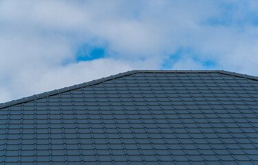 Dark gray modern roof tiles showing an angled edge under a bright blue sky with white clouds.