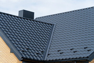 Dark grey metal roof tiles on a modern house with chimney and light brick wall. © SMK