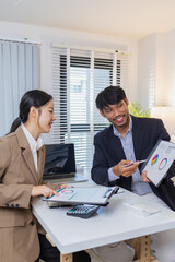 Business colleagues are engaged in a collaborative discussion, analyzing financial charts and reports on the wall and table. They exchange ideas, review strategies, and plan future goals.