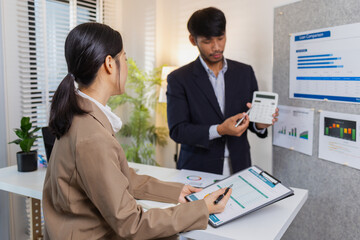 Business colleagues are engaged in a collaborative discussion, analyzing financial charts and reports on the wall and table. They exchange ideas, review strategies, and plan future goals.