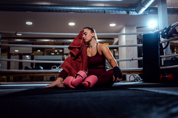 Tired female boxer sitting in boxing ring resting after training.