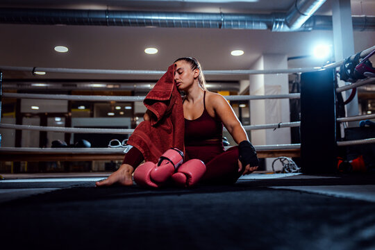 Tired female boxer sitting in boxing ring resting after training.