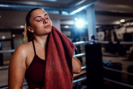 Tired female boxer standing in boxing ring resting after training.