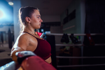 Female boxer leaning against the ropes of a boxing ring resting after training.