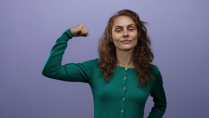 Confident woman with curly hair raising fist in empowerment pose against isolated purple wall...