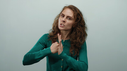 Woman expressing anger gesturing aggressively against white background wearing green sweater with...