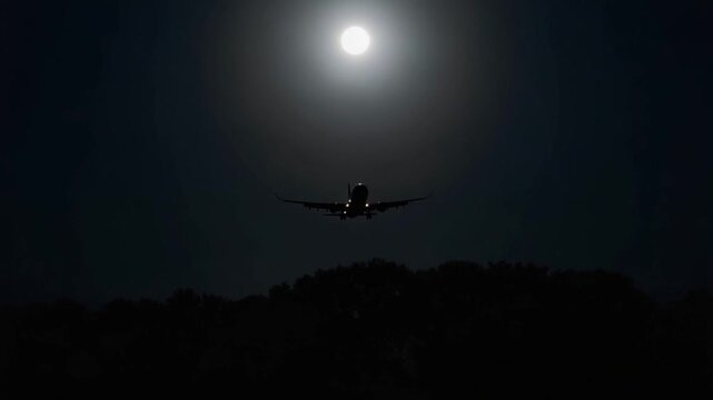Airplane landing lights gradually approaching luminous full moon, casting silhouetted tree outline against dark nighttime sky with moonlight glowing softly
