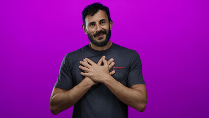 Hispanic man with beard expressing emotion with hands on chest against vibrant purple background...