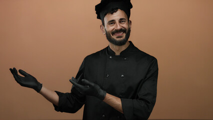 Hispanic man in black chef uniform with a beard extends hands presenting something against an...