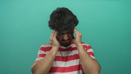 Young man with beard in striped shirt looking stressed against green background.