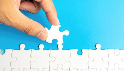 Hand placing the final piece of a white jigsaw puzzle against a blue background, completing a conceptual representation of solution and accomplishment