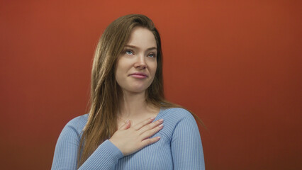 Fototapeta premium Woman looks up in studio wearing blue sweater against red background with calm demeanor; uncertainty.