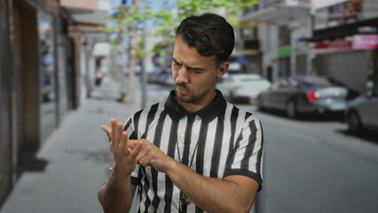 Young hispanic man referee on city street counting fingers thoughtfully while standing in outdoor...