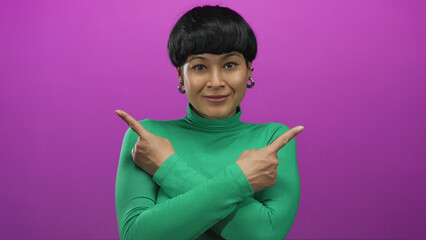 Woman smiling and pointing in opposite directions against an isolated pink background wearing a...