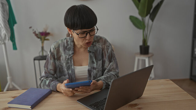 Woman using tablet in modern living room with laptop on table surrounded by books and plants