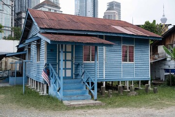 A traditional blue house located in Kampung Baru, with modern buildings in the background.