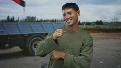 Hispanic man in green sweater dancing with raised arms in front of a truck on a city street under cloudy sky; joy freedom.