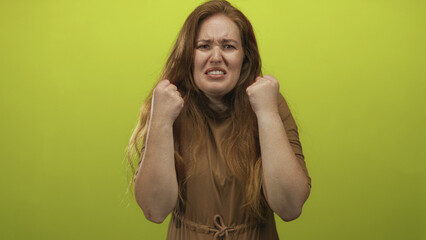 Woman with long red hair and open mouth yelling intensely in studio against a lime green...