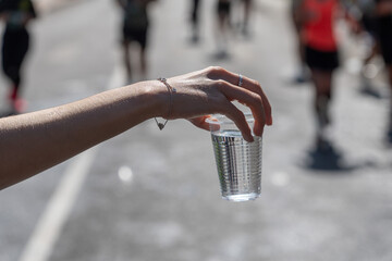 A close-up of a volunteer's hand offering a cup of water to a marathon runner