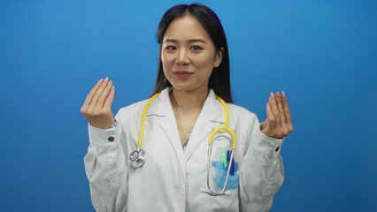 Young chinese woman doctor in uniform with stethoscope making money gesture over blue background.
