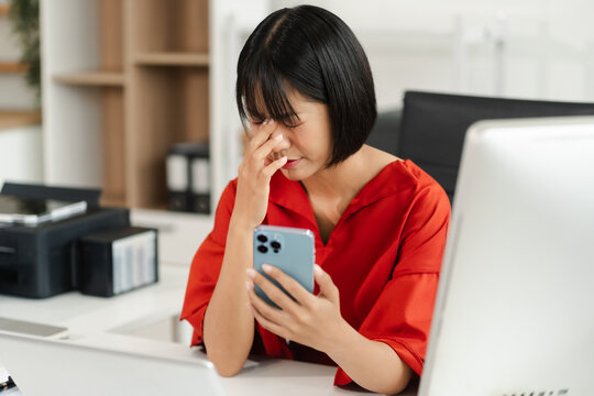 Young sad businesswoman is sitting at table, covering his face with his hand and talking on cell phone. On desk is laptop, tablet computer, Stress. - Powered by Adobe