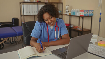 Woman writing notes in notebook with blue pen at clinic desk beside an open laptop; quiet concentration.