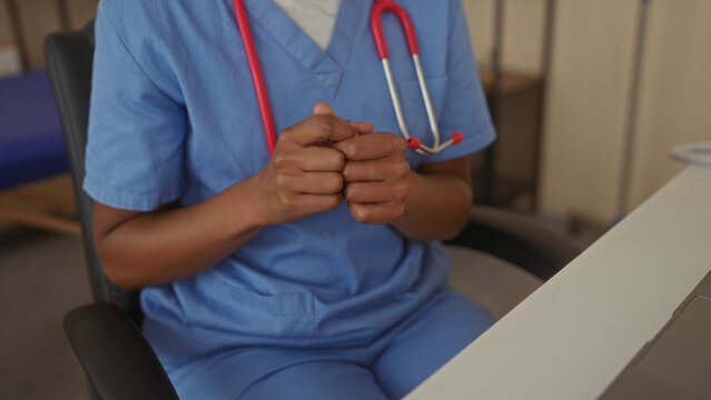 African american woman in blue scrubs wearing stethoscope touches finger on clinic desk; compassion.