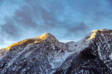 Golden sunlight highlights snowy mountain ridges against a crisp blue sky, capturing the...