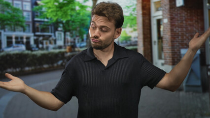 Fototapeta premium Man shrugging with palms up and finger pointing to chest on a city street beside a brick building doorway; playful skepticism doubt.