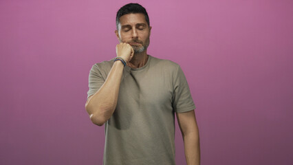 Man with hand on chin and closed eyes wearing beige t shirt and bracelets in studio against pink...