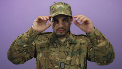 Hispanic soldier man in camouflage uniform with dogtags points finger to camera in purple studio;...